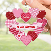 Heart-shaped keychain with 'Grandma' and 'Sofia' text, held by a hand against a blurred green background.