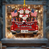 Personalized Christmas ornament shaped like a red pickup truck carrying three snowman children, American flags, gifts, and a gold hanging loop, displayed in front of a warmly lit snowy window scene.